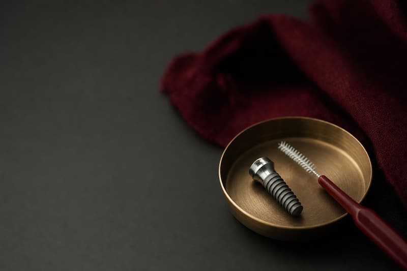 Implante dentário de titânio em uma pequena bandeja de latão, ao lado de uma escova interdental